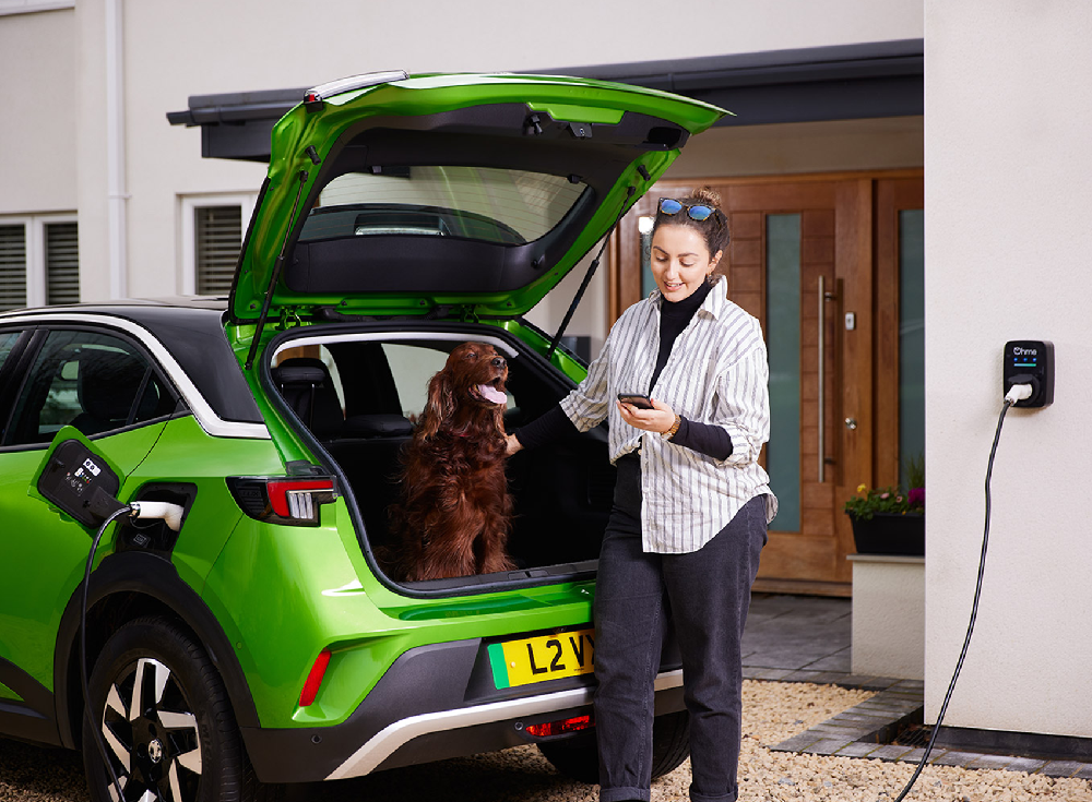 Driver controlling the Ohme ePod via the Ohme app on a smartphone while the EV charges